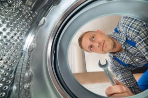 repairman with spanner looking inside the washing machine