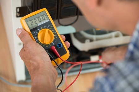 repairman checking fridge with digital multimeter