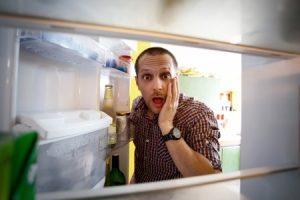 Shocked men looking in his empty fridge.