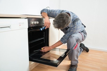 repairman examining oven with flashlight